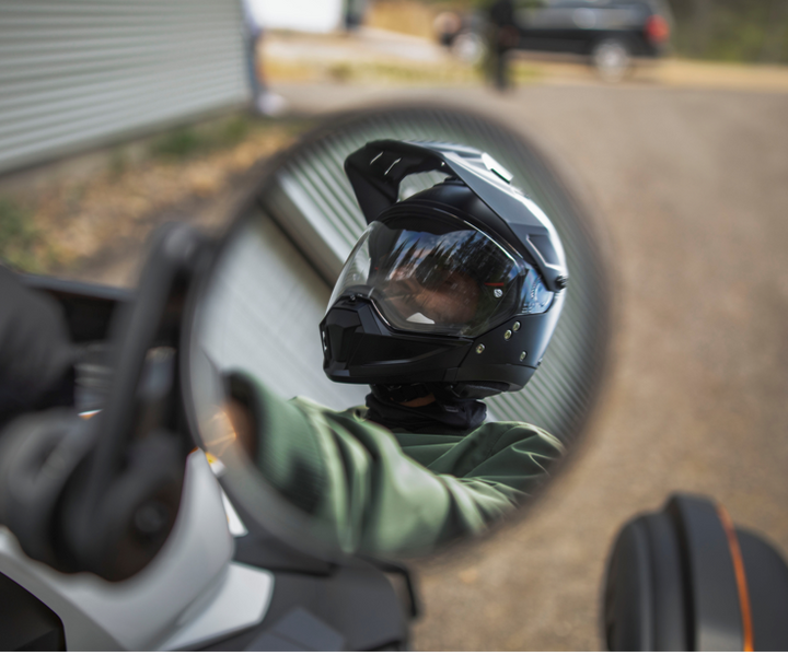 reflection of man in mirror with a helmet on, riding his on-road vehicle. 